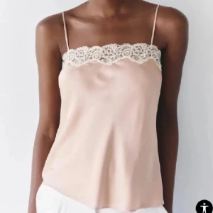 Rosa/champagnefärgad linnetopp med spets - Säljer en champagnefärgad linnetopp i satin med tunna axelband och vacker spetsdetalj längs urringningen. Perfekt för dig som gillar en stilren och feminin look. Toppen har en mjuk glans och faller snyggt.