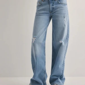 Ljusblå wide jeans med slitningar - Säljer ett par ljusblå jeans med loose fit ch snygga slitningar på låren och knäna. Jeansen har klassisk femficksmodell, låg midja och är tillverkade i denim. Perfekta för en avslappnad och trendig look.