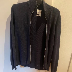 Svart stickad kofta från Dobber - Mörk, stilren stickad kofta från Dobber i svart med hel dragkedja framtill och hög krage. Perfekt för lager-på-lager och passar till många olika outfits. Långärmad och ribbad vid muddar och krage.