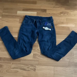 Blå jeans från G-Star RAW - Snygga blå jeans från G-Star RAW med klassisk femficksdesign och coola detaljer som metallogo och patch bak. Jeansen har raka ben och tydliga kontrastsömmar. Perfekta för dig som gillar streetwear och vill ha en tidlös look.