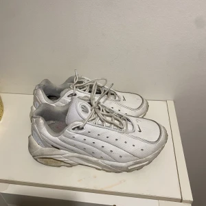 Vita Nike sneakers i skinn, strl 42 - Snygga vita Nike sneakers i skinn med perforerade detaljer och klassisk snörning. Modellen har en chunky sula och grå meshfoder för extra komfort. Perfekta för dig som gillar en clean och sportig look.