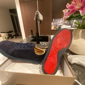 Mörkblå sneakers från Christian Louboutin - Snygga mörkblå sneakers från Christian Louboutin i mocka med klassisk röd sula och diskret logga. Skorna har rund tå, platt sula och blå snörning. Insidan är ljusbeige och materialet känns lyxigt och mjukt. Perfekta för dig som vill sticka ut med exklusiva detaljer. Hör av dig vid minsta fundering 🤗
