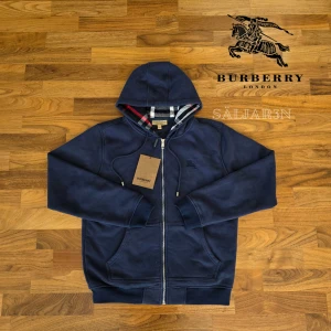 Marinblå Burberry Hoodie  - Letar du efter en stilren och lyxig hoodie? Denna helt nya marinblåa Burberry-hoodie kombinerar elegans med hög komfort. Den har Burberrys ikoniska rutmönster i fodret och en diskret logga på bröstet för en exklusiv touch. Liten i storleken! Tillverkad av mjukt, slitstarkt material och utrustad med dragkedja samt huva – både praktisk och stilfull.  📌 Skick: Ny med taggar. 📦 Snabb leverans – skickas samma dag