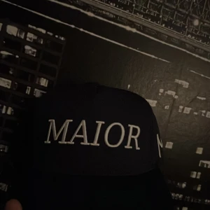 Svart keps MAIOR 2023 brodyr - Snygg svart keps med vit brodyrtext 'MAIOR' framtill och siffrorna '20' och '23' baktill. Klassisk form med böjd skärm och justerbar passform. Perfekt accessoar för en cool och stilren look.