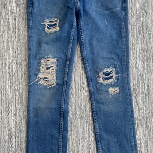 Levi's Patty Anne ripped jeans blå - Snygga blå Levi's Patty Anne jeans med slim fit och square-cut. Jeansen har flera slitna och trasiga detaljer framtill för en cool, edgy look. Klassisk femficksmodell med dragkedja och knapp. Perfekta för dig som gillar streetstyle.