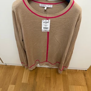 Beige stickad tröja med rosa detaljer - Beige stickad tröja från My Perfect Jumper med långa ärmar och rosa detaljer vid halsringning, ärmslut och nederkant. Tröjan har en normal passform och är perfekt för en enkel men ändå färgglad look.