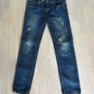 Levi's 511 Slim Straight jeans blå - Säljer ett par Levi's 511 Slim Straight jeans i mörkblå denim med slitna detaljer och snygga slitningar på benen. Klassisk modell med orange sömmar och läderpatch bak i midjan. Perfekta för dig som gillar en smalare rak passform.