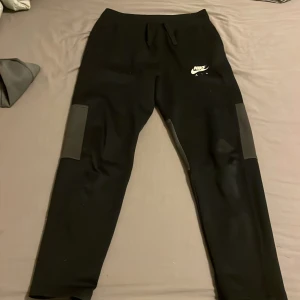 Svarta Nike Air mjukisbyxor XL - Svarta mjukisbyxor från Nike Air i storlek 158-170, med vit logga på låret och snygga paneldetaljer på knäna. perfekt för chill eller träning.