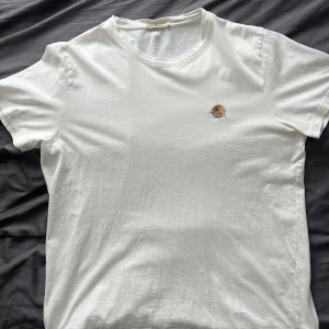 Vit t-shirt från Nudie Jeans Co - Vit t-shirt från Nudie Jeans Co i mjuk bomull. Klassisk rund hals och korta ärmar. På bröstet finns ett broderat motiv med palm, solnedgång och hav. Nypris: 599kr, Skick: 9/10!