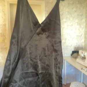 Svart långklänning med öppen rygg - Säljer en svart långklänning med djup v-ringning och öppen rygg. Klänningen har en elegant silkesliknande yta och tunna axelband. Perfekt för dig som vill ha en stilren och sofistikerad look. Passformen är normal och klänningen faller snyggt längs kroppen.