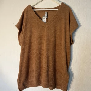 Brun frottéklänning från Lindex - Säljer en chill brun klänning från Lindex i mjuk frotté. Den har v-ringad hals, ärmlös design och loose passform som ger en avslappnad vibe. Perfekt för varma dagar och enkel att styla med sneakers eller sandaler. Ny med prislapp!