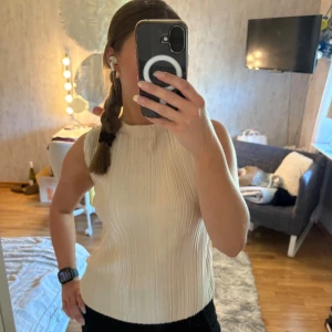 Plisserad ärmlös topp från Stockh LM - Säljer en snygg plisserad topp från Stockh LM i en ljus beige nyans. Toppen är ärmlös med rund halsringning och har ett glansigt tyg som ger en lyxig känsla. Perfekt att styla med både jeans och kjol för en trendig look. Toppen är köpt på MQ och är använd en gång.