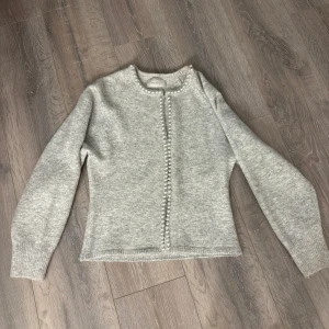 Grå kofta med pärldetaljer Neo Noir - Superfin ljusgrå kofta från Neo Noir med pärlor längs halsringning och hela knappslån. Storlek S men funkar som Xs.Använd typ 2-3 gånger så mycket bra skick 💞kan tänka mig sänka priset lite om man kommer med förslag 🥰