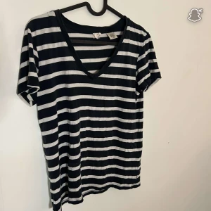 Randig t-shirt från Levi's med v-ringning - Snygg svart och vit randig t-shirt från Levi's i storlek S. T-shirten har v-ringad hals och korta ärmar, perfekt för en chill och avslappnad stil. Materialet är mjukt och skönt, troligtvis bomull. Passar dig som gillar klassiska mönster och streetwear.