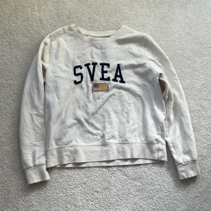 Vit sweatshirt från Svea med tryck - Vit sweatshirt från Svea i storlek XS med broderat SVEA-tryck och en liten flagga på bröstet. Tröjan har rund hals, långa ärmar och ribbade muddar. Mjuk och skön bomullskvalitet, perfekt för chill dagar eller när du vill ha en enkel och clean look.