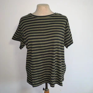 Randig t-shirt från lager 157 - Snygg t-shirt med olivgröna och svarta horisontella ränder från lager 157. Modellen har rund hals och korta ärmar, perfekt för en chill och avslappnad stil. Materialet känns mjukt och lätt, troligtvis bomull. Passformen är normal och funkar till många olika outfits.