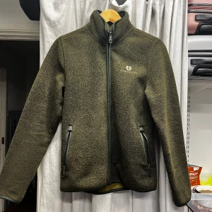 Mörk grön fleecejacka från Chevalier - Säljer en mörk grön fleecejacka från Chevalier med hel dragkedja och två fickor med dragkedja. Jackan har hög krage. 