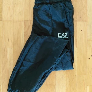 Svarta täckbyxor från EA7 Emporio Armani - Säljer ett par svarta täckbyxor från EA7 Emporio Armani. Byxorna har elastisk midja, diskret logga på benet och meshfoder på insidan. Perfekta för kalla dagar när du vill hålla stilen och värmen. Storlek:M