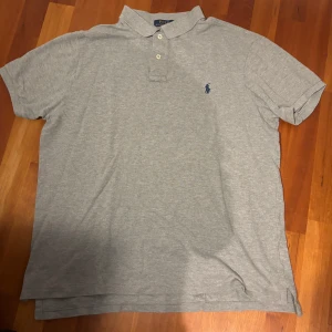 Grå pikétröja Polo Ralph Lauren - Snygg grå pikétröja från Polo Ralph Lauren. Piken är i storlek XL, men den passar som L/M. Den är alltså rätt bred, men inte för lång.