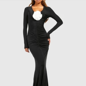 Svart långklänning med vit blomma - Supersnygg svart långklänning med figurnära passform. Den är aldrig använd, köpte den för att ha på en förlovning men slutade med att jag tog en annan klänning istället. Den är helt slutsåld! 