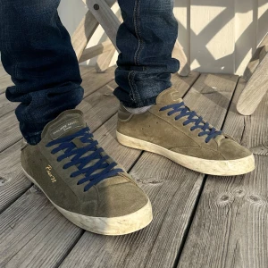 Philippe Model - Snygga Philippe Model sneakers i olivgrön mocka med mörkblå snörning och vit sula. Guldfärgad text på sidan. Perfekta för dig som gillar stilrena och trendiga skor med en unik touch.