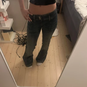 Mörkblå bootcut jeans med låg midja - Säljer ett par mörkblå jeans med snygga slitningar och bootcut-ben. Jeansen har låg midja, klassiska fickor och dubbla knappar framtill. Storlek 24/32
