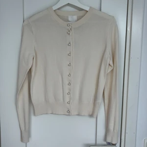 Cremevit kofta med pärlknappar från H&M - Superfin kofta från H&M med pärlknappar framtill. Klassisk rund halsringning och långärmad modell i mjukt stickat material. Perfekt att slänga över en topp för en clean och stilren look.