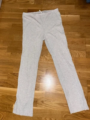 Ljusgrå ribbade mjukisbyxor - Säljer ett par ljusgrå ribbade mjukisbyxor med raka ben och stretchig midja. Byxorna har en enkel och clean look, perfekta för chill dagar hemma eller när du vill vara bekväm. Materialet är mjukt och följsamt.