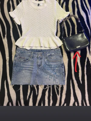 Svart axelväska från Urban Outfitters - Snygg svart axelväska från Urban Outfitters med croco-mönstrad yta och kedjedetalj på axelbandet. Väskan har en stilren, rektangulär form och en metallbricka med logga framtill. Perfekt för dig som vill ha en trendig accessoar.