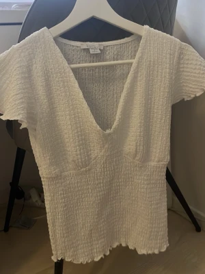 Vit ribbad blus från Amisu - Supersöt vit blus från Amisu i storlek S. Toppen har ribbad struktur, v-ringning och korta ärmar med lätt volangkant. Perfekt till sommaren och enkel att styla med jeans eller kjol. Materialet känns mjukt och luftigt.