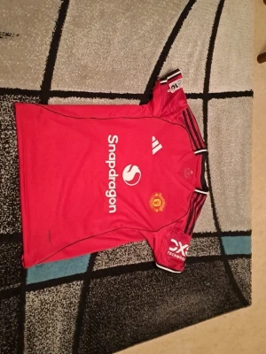 Manchester United matchtröja Adidas M - Säljer en röd Manchester United matchtröja från Adidas i storlek M. Tröjan har svarta och vita detaljer, klubbmärke på bröstet, sponsorloggor och svarta ränder på axlarna. Slim fit-modell i polyester, perfekt för fotboll eller att bära som supporter. Säljs för 450 kr. Först till kvarn som gäller. Tveka inte att kontakta om du är intresserad eller har några frågor!