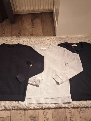 Grå ribbad långärmad tröja H&M - Säljer en grå långärmad tröja från H&M i storlek 158/164. Svarta tröjan längst åt vänster är i storlekwn 152/158. Tröjan är ribbad med rund hals och har en enkel, stilren look som passar perfekt till jeans eller mjukisbyxor. Skön och mjuk bomullskvalitet.
