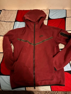 Nike tech vinröd  - Säljer en vinröd Nike Tech Fleece kofta i fint skick. Bekväm och stilren med modern passform. Perfekt till vardags eller streetwear. Inga hål eller fläckar.