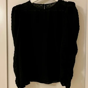 Svart blus i mesh från Zara, S/M - Fin svart blus i mesh med fina detaljer, kan både kläs upp och ned beroende på tillfälle. Tunn med svarta prickar i tyget, se foton. Ärmen är lite vidare upptill och ger fin form på blusen. Ett band på axeln som kan knytas efter smak. Mycket bra skick. Storlek S/M beroende på hur man vill ha passformen. 100 % polyester.