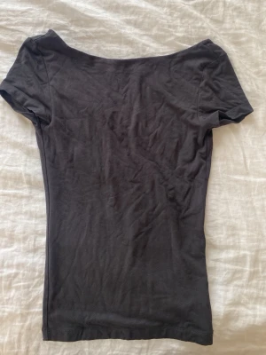 Grå topp med öppen rygg - Säljer en grå, tight topp i mjuk bomull med korta ärmar och en djup, öppen rygg. Enkel och stilren design som passar perfekt till jeans eller kjol.