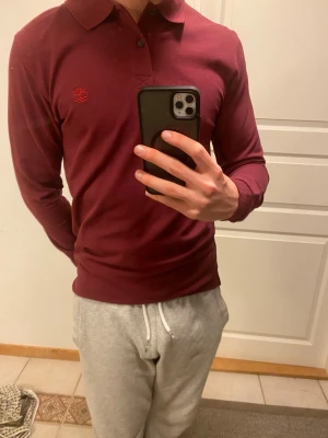 Vinröd långärmad Timberland skjorta - Säljer en vinröd långärmad skjorta från Timberland i slim fit. Skjortan har klassisk krage, två knappar framtill och broderad Timberland-logga på bröstet. Materialet är 100% bomull och känns mjukt mot huden. Perfekt för dig som gillar stilrena och enkla plagg.