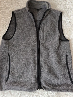 J.Lindberg Grå ullväst - Säljer en grå ullfleeceväst från J.Lindeberg med svart kantband, hög krage och hel dragkedja framtill. Västen har praktiska fickor och en stilren look med diskret logga på ryggen. Perfekt lager för kyliga dagar. Pris kan diskuteras 