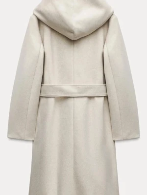 Beige kappa med huva från Zara - Snygg beige kappa från Zara med stor huva och knytskärp i midjan. Kappan har långa ärmar, två fickor fram och en clean, look. Perfekt för dig som vill ha en stilren och mysig jacka till höst och vinter.