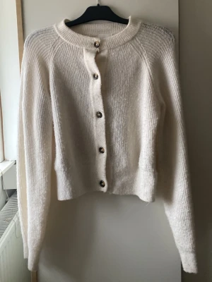 Vit stickad kofta från H&M - Supermysig vit stickad kofta från H&M i storlek S. Koftan har långa ärmar, rund halsringning och snygga knappar framtill. Perfekt att slänga på sig när det är kyligt ute och passar till allt. Enkel och stilren design som är lätt att matcha.