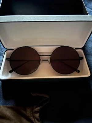 Oanvända solglasögon från Corlin - Säljer ett par riktigt snygga svarta solglasögon i retro design, med runda glas. Perfekt för dig som vill ha en clean och modern look. Kommer i originalförpackning med tillhörande fodral. Nypris ca 1300kr.