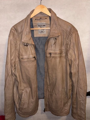 Beige skinnjacka från Angelo Litrico - Säljer en beige skinnjacka från Angelo Litrico med coola detaljer som dragkedjor på bröstfickorna och klassisk krage. Jackan har en snygg, avslappnad passform och är perfekt för dig som vill ha en stilren look med edge.