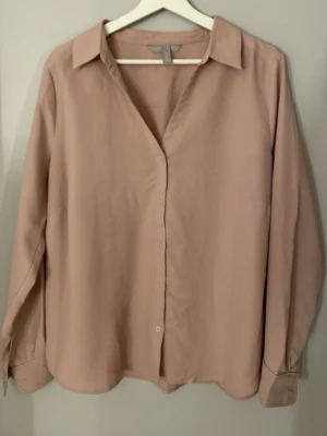 Ljusrosa skjorta med knappar - Säljer en stilren ljusrosa skjorta från H&M i storlek 48. Skjortan har klassisk krage, långa ärmar och knäppning framtill. Materialet känns mjukt och flowy, perfekt för en clean och enkel look.