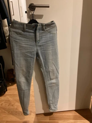 Ljusblå skinny jeans från Dondup - Säljer ett par ljusblå skinny jeans från Dondup i storlek 28. Jeansen har klassisk femficksdesign, bälteshällor och snygga slitningar för en avslappnad look. Tillverkade i mjukt denimtyg med gul kontrastsöm och Dondup-läderpatch bak i midjan.