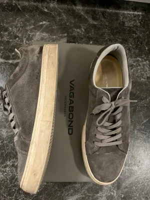 Vagabonds mockaskor  - Snygga grå sneakers från Vagabond i mjuk mocka med matchande grå snörning och vit sula. Skorna har en klassisk rund tå och platt sula, perfekt för en clean och stilren look. Passar till både jeans och chinos för en avslappnad vibe.