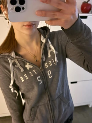 Hoodie zip up Abercrombie unik - Grå Abercrombie & Fitch-hoodie med dragkedja i vintagestil. Storlek M passar en vanlig S bättre! I toppskick! Har den vita Abercrombie & Fitch-logotypen i paljetter över bröstet.