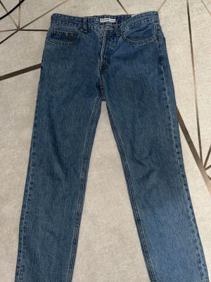 Blå regular fit jeans 30/30 - Klassiska blå jeans i regular fit med raka ben och femficksmodell. Jeansen har en enkel design med knappgylf och bälteshällor. Perfekta för dig som gillar en tidlös och avslappnad stil. Materialet är tåligt denim i bomull.