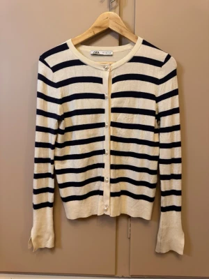 Randig kofta från Zara, marinblå/vit - Säljer en klassisk randig kofta från Zara i marinblått och vitt. Koftan har rund hals, långa ärmar och pärlknappar framtill. Tillverkad i mjukt stickat material, perfekt för lager på lager under höst och vår.