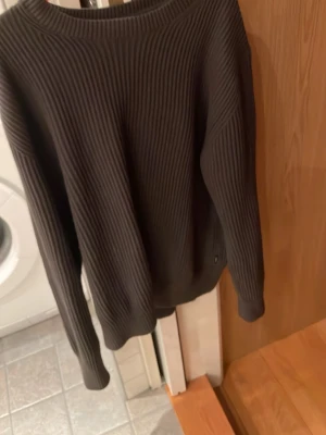 Mörkbrun ribbad stickad tröja - Säljer en mörkbrun stickad tröja med ribbad struktur. Tröjan har rund halsringning och långa ärmar, perfekt för kyligare dagar. Enkel och stilren design som passar till det mesta.