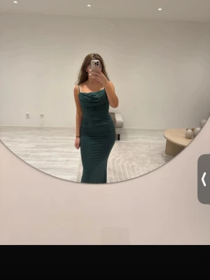 Mörkgrön långklänning med drapering - Säljer en elegant mörkgrön långklänning med smala axelband och snygg drapering vid bysten. Klänningen har figurnära passform och är perfekt för speciella tillfällen. Materialet känns mjukt och följsamt mot kroppen. Är även en inbyggd korsett skulle nog säga att det är en S/M