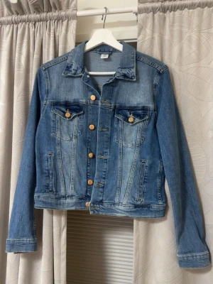 Klassisk blå jeansjacka - Snygg blå jeansjacka med klassisk passform och kontrastsömmar. Jackan har två bröstfickor med lock och knappar, samt sidofickor. Långa ärmar med knapp vid ärmslut och knappar framtill. Perfekt basplagg till garderoben.